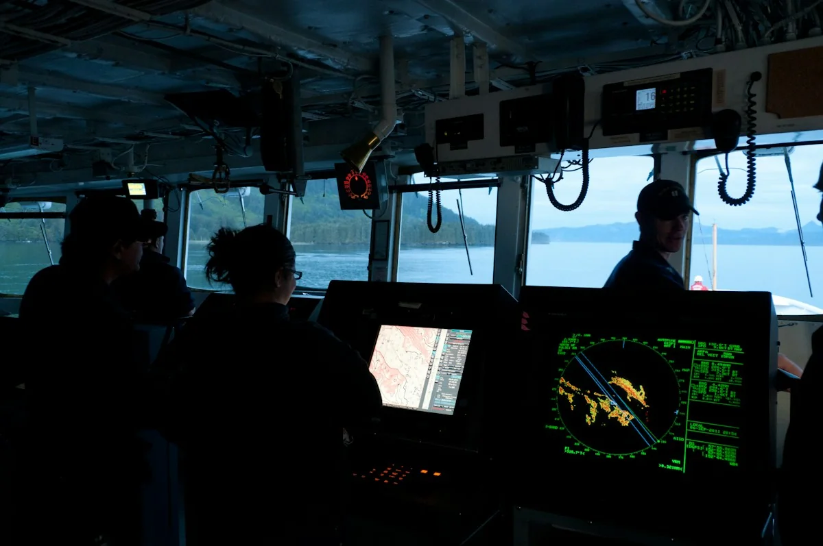 Maritime personnel working with navigation equipment on a vessel’s bridge